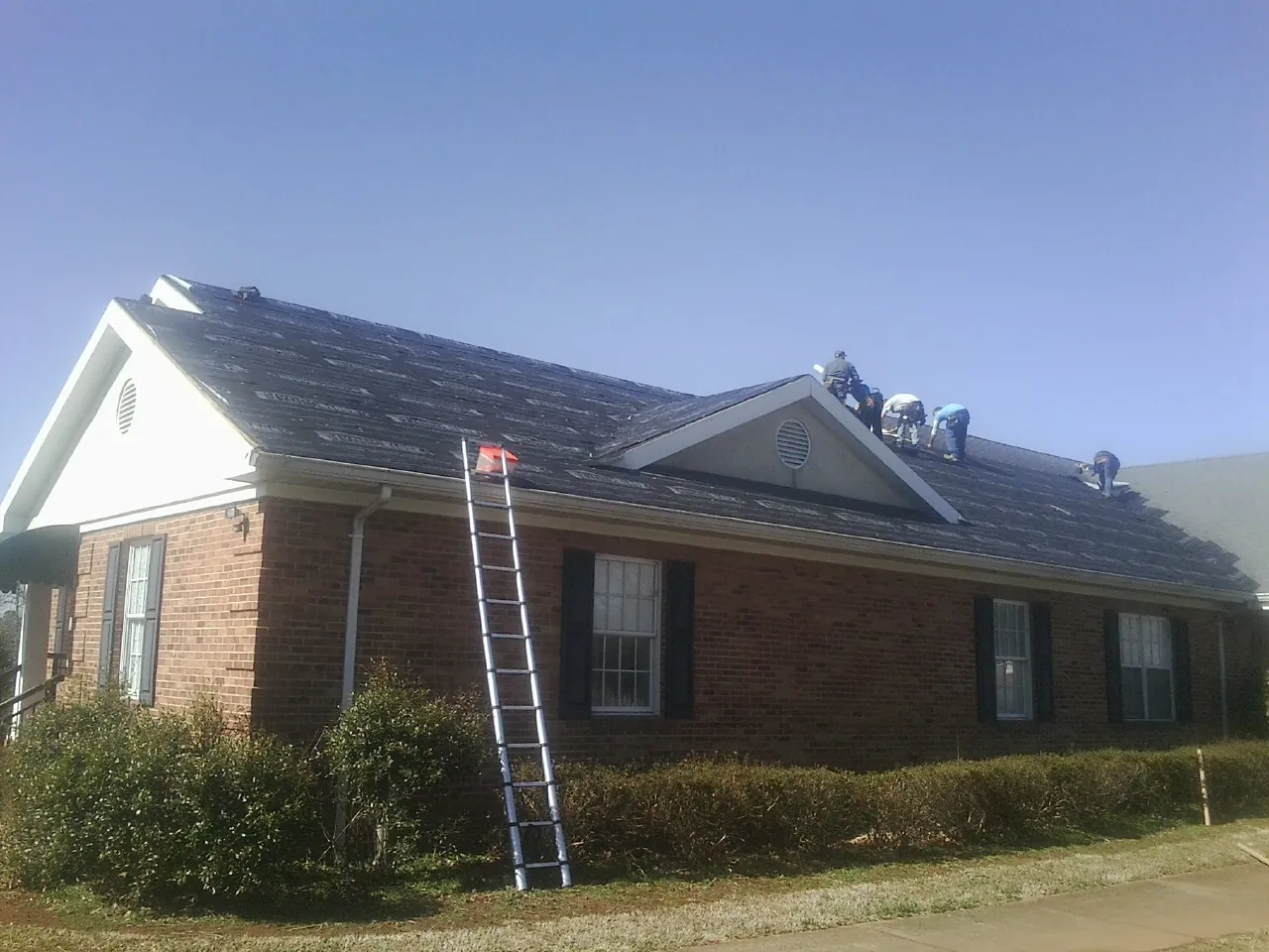 Crew tearing shingles off a brick ranch roof with a ladder set — Metal Roof Repair work by our crew in Conway
