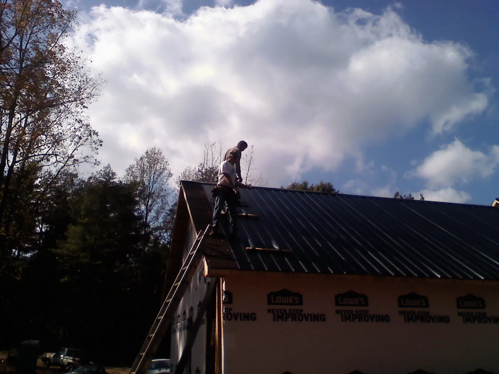 Roofer fastening dark metal panels high against a cloudy sky, from a Roof Inspection job in Conway